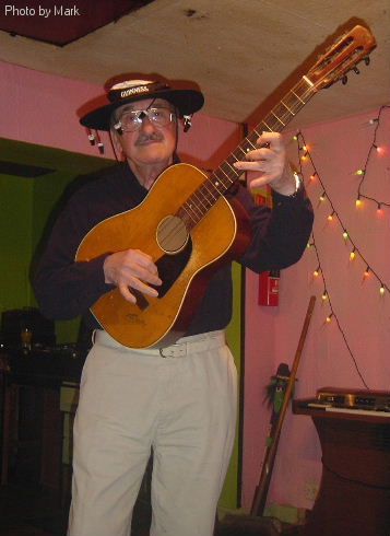 Gordon Cragg standing up holding the guitar like a spanish flamenco virtuoso while wearing a wide brimmed guinness rugby world cup hat with aussie type pretend corks to add just that touch of class.